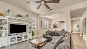 Un salón espacioso con un sofá seccional gris grande, un televisor de pantalla plana sobre un mueble blanco y un ventilador de techo.