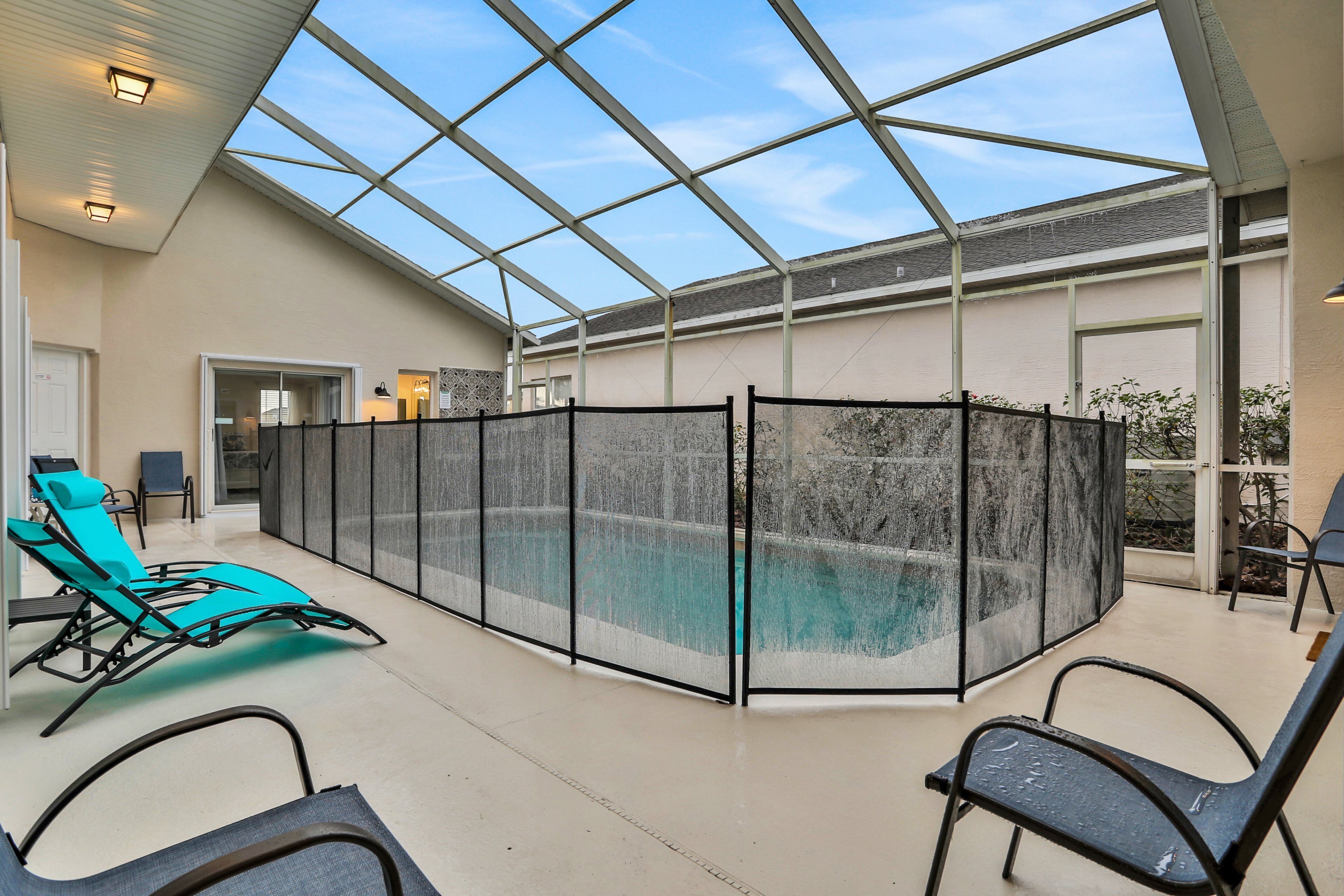 A covered swimming pool area with lounge chairs and a glass enclosure.