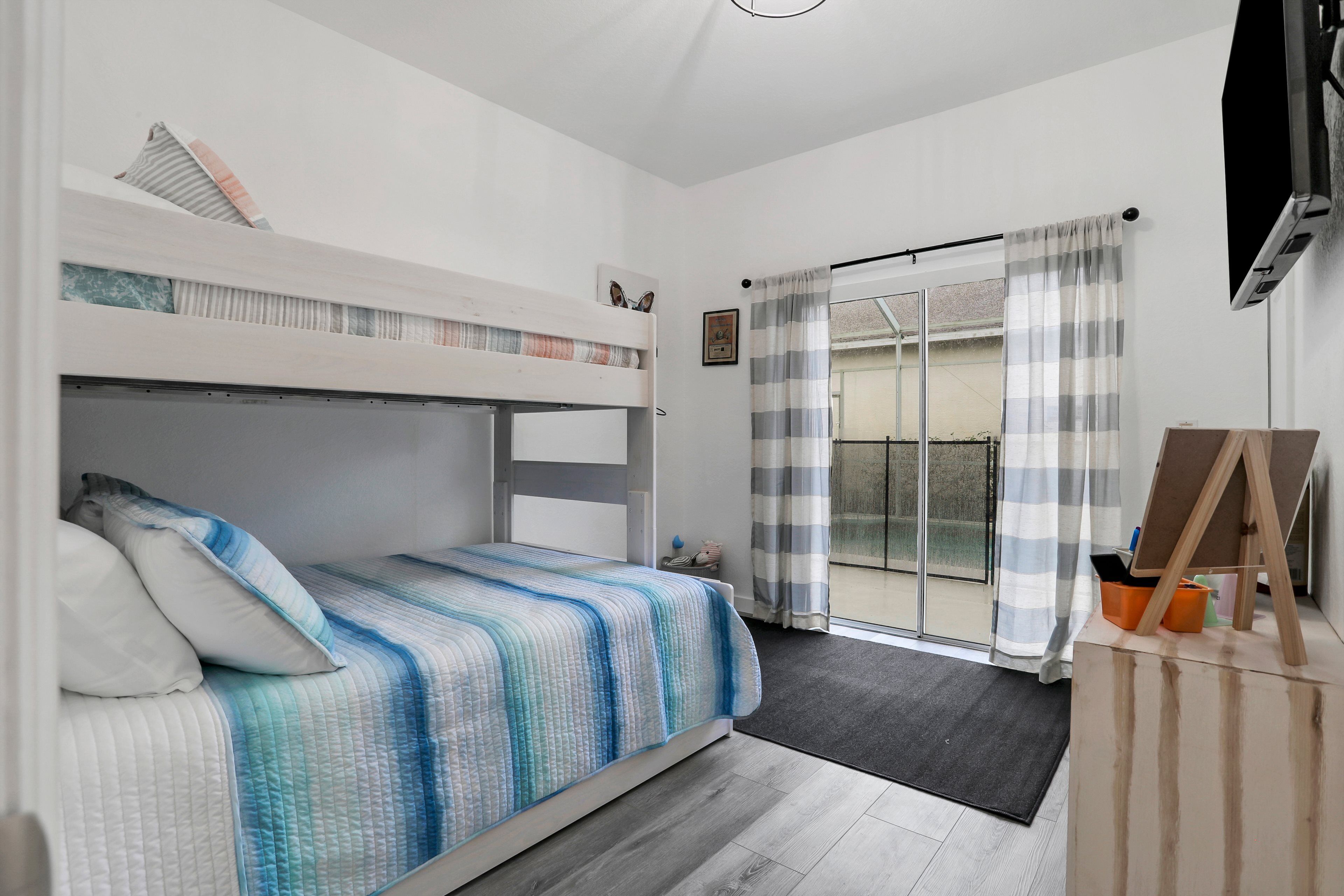 A bedroom with a bunk bed, a large window with curtains, and a painting on the wall.