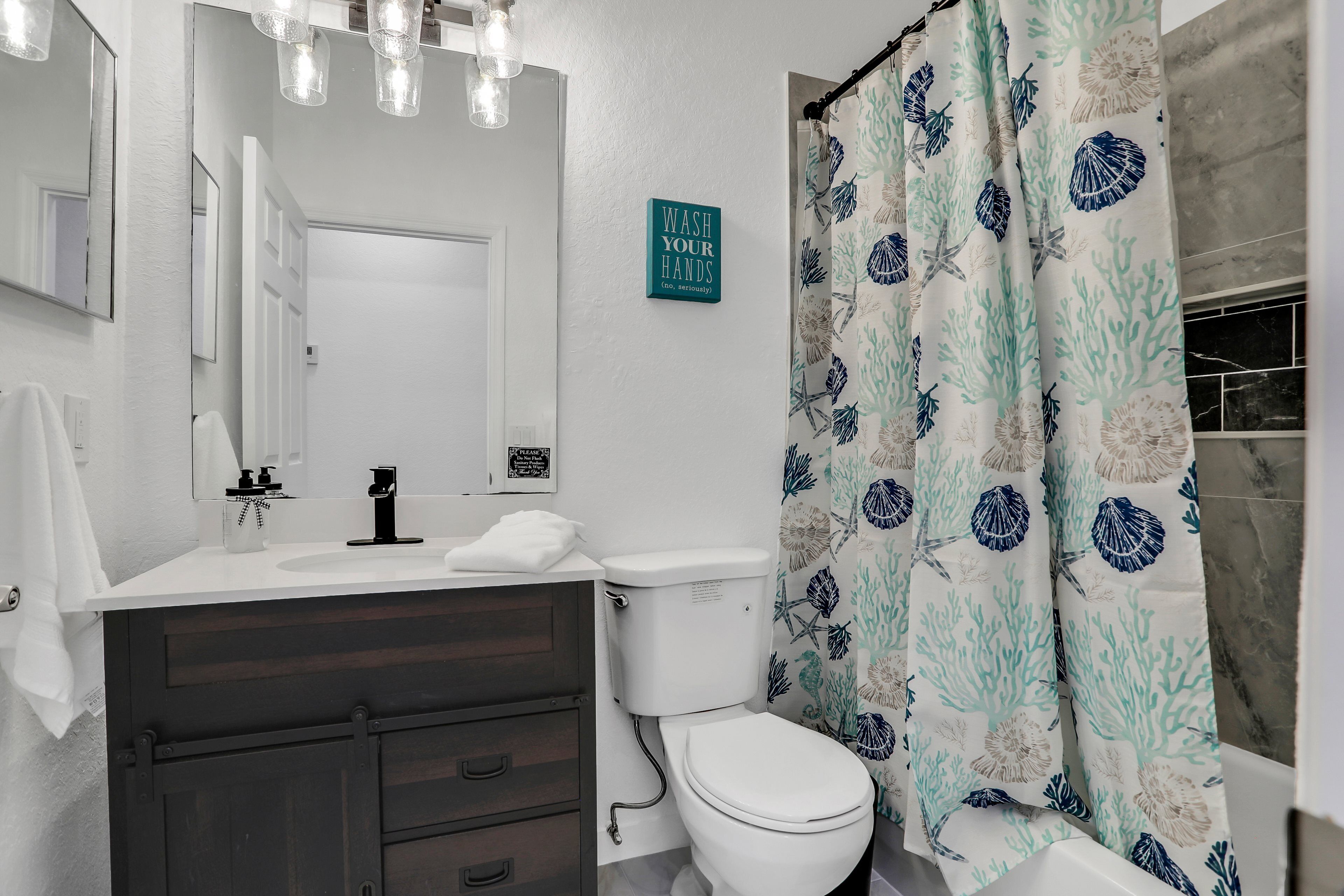 A bathroom with a white sink, dark wooden cabinet, white toilet, and a shower curtain with a sea shell pattern.