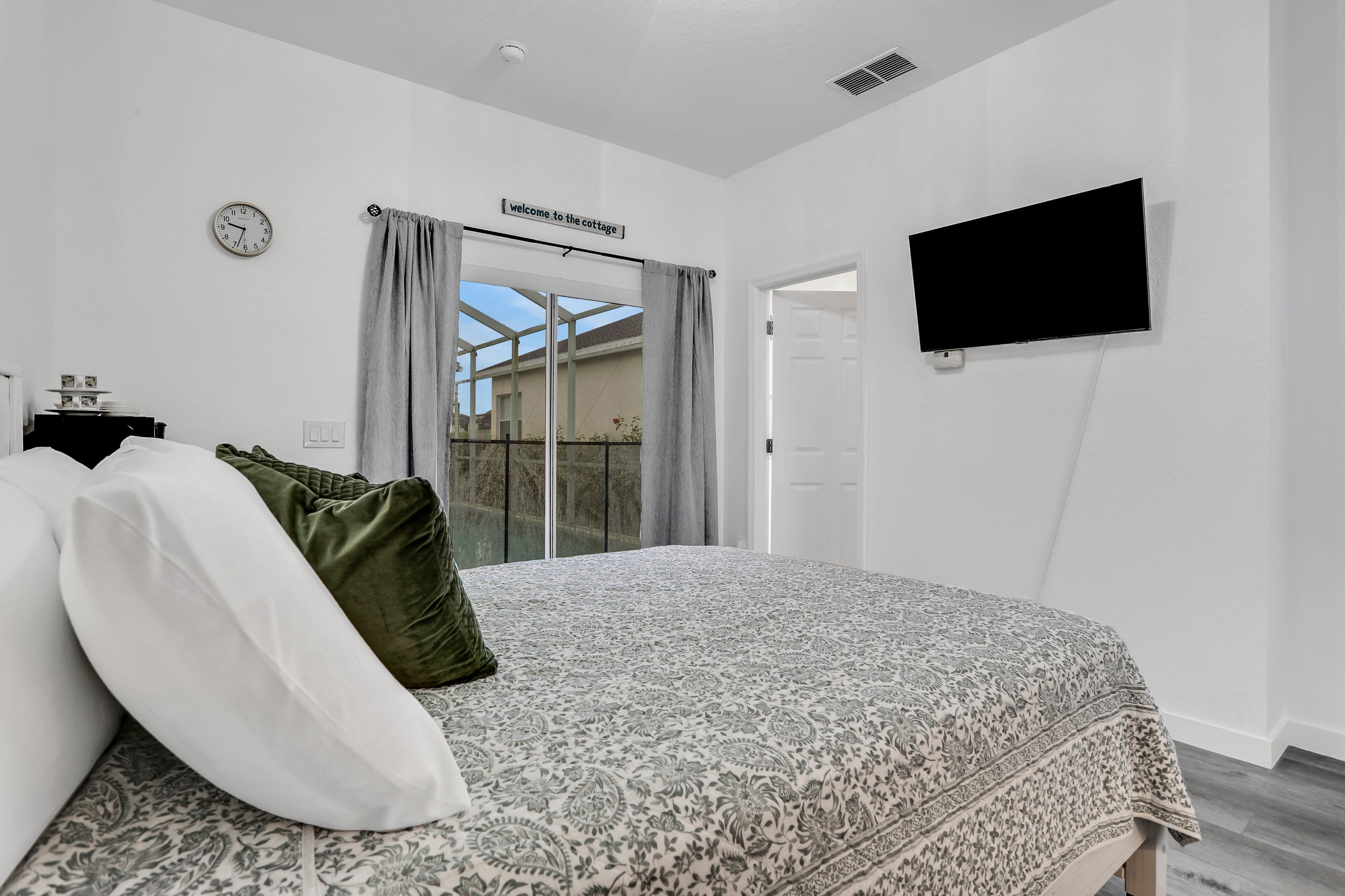 A bedroom with a bed, a TV, a clock, and a sign that reads "Welcome to the cottage."