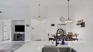 A modern kitchen with a large island, a sink, and a dining area with chairs and a table. - WH485WP - Game Room | Private Pool | Newly Remodeled/Upgraded (Davenport)