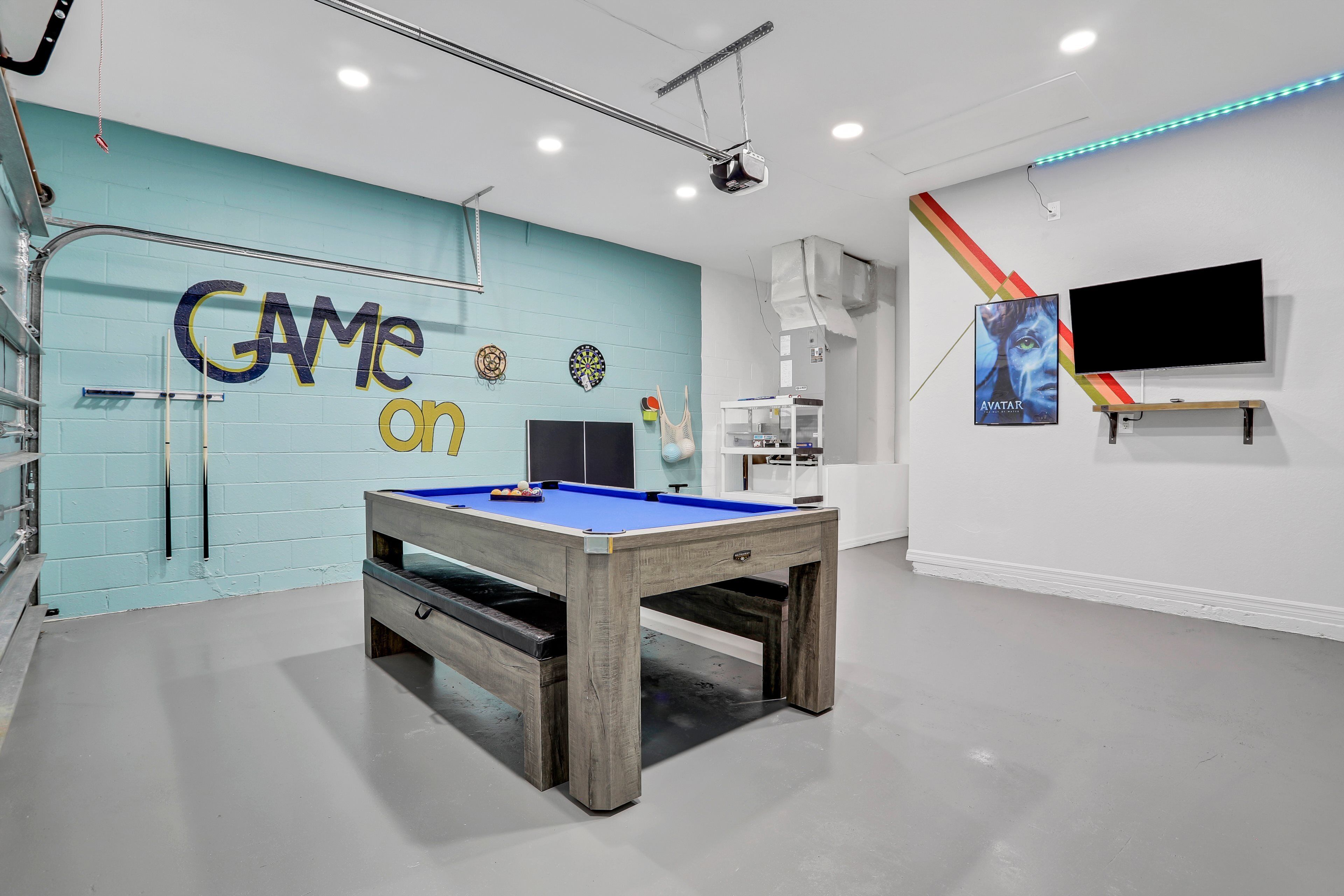 A pool table in a room with a blue wall and a dartboard.