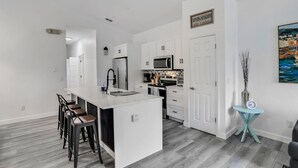 A modern kitchen with white cabinetry, a central island with bar stools, a microwave, and a refrigerator. - WH485WP - Game Room | Private Pool | Newly Remodeled/Upgraded (Davenport)