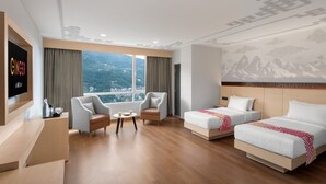 Ein Hotelzimmer mit großem Fenster, zwei Einzelbetten, einem Schlafsofa, einem Fernseher und einem kleinen Tisch.