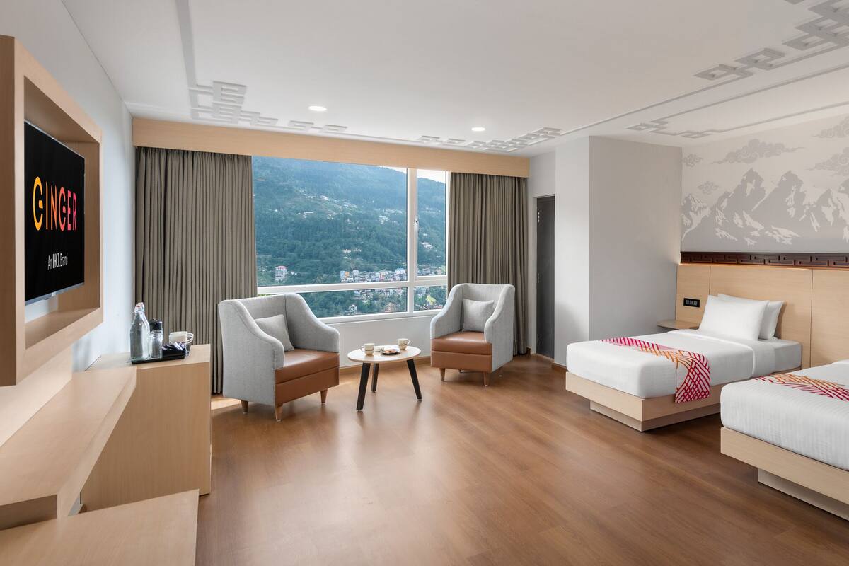 A hotel room with a large window, two single beds, a sofa, a TV, and a small table.