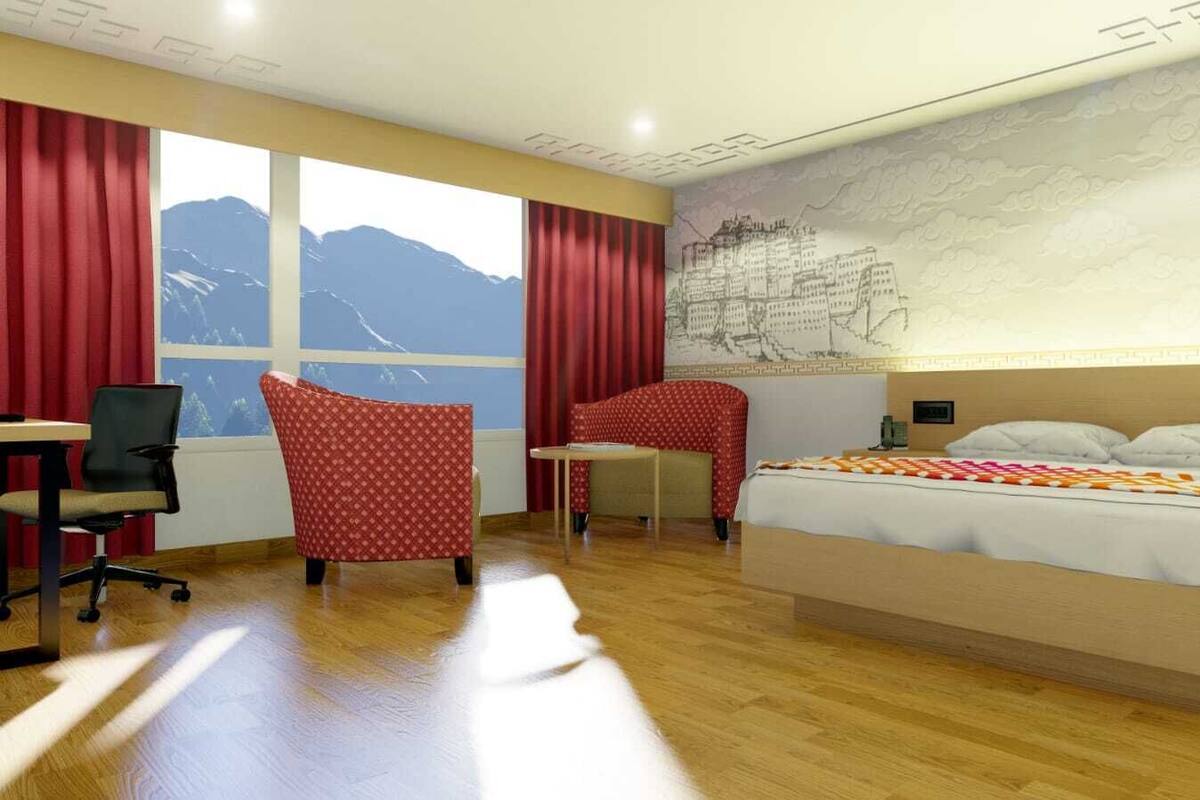 A hotel room with a bed, two red chairs, a desk, and a large window with a mountain view.