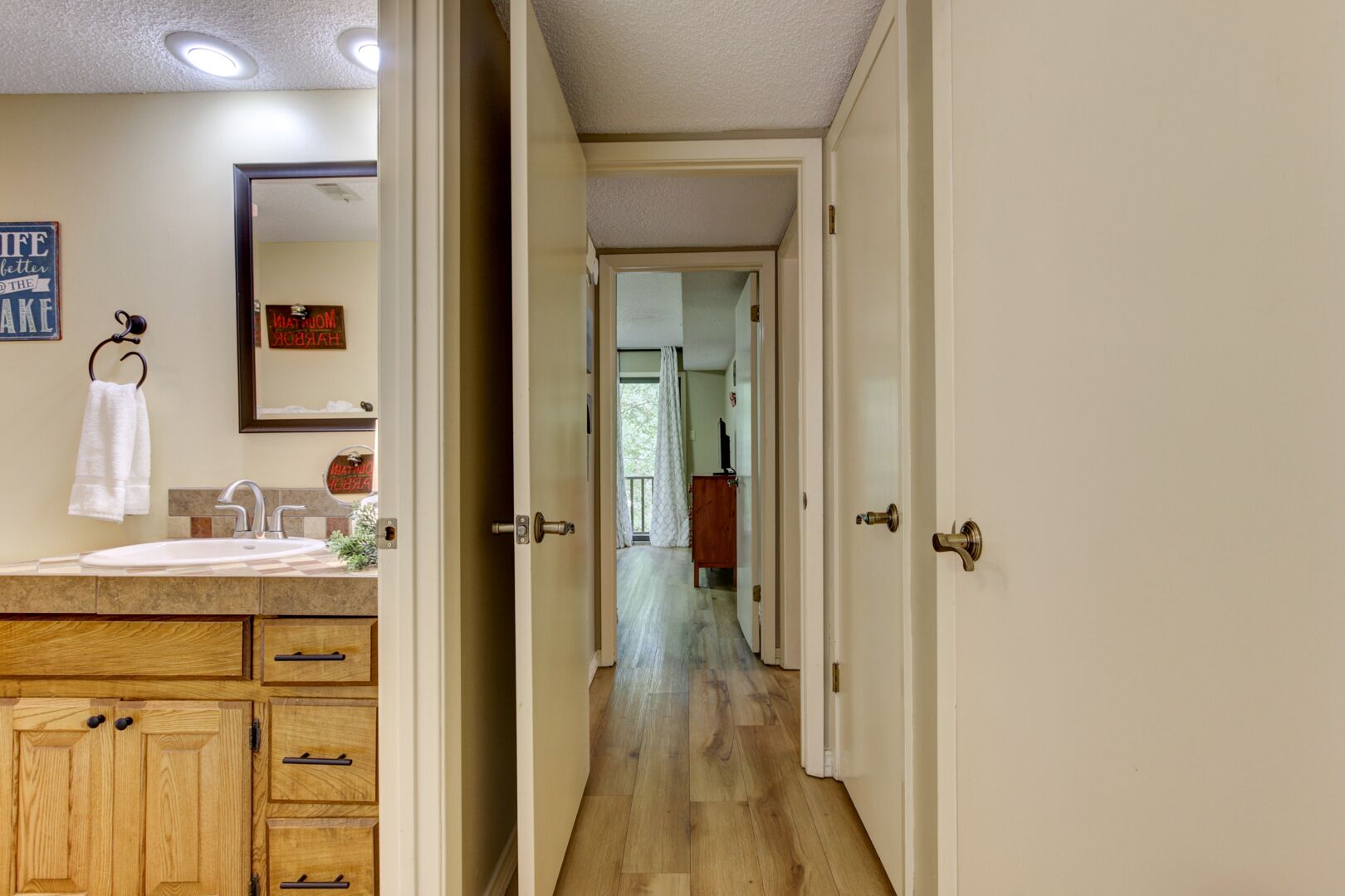 Un pasillo que conduce a un baño con lavabo, armarios de madera y un espejo.