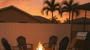 Une terrasse avec un foyer entouré de chaises, un barbecue et des palmiers en arrière-plan.