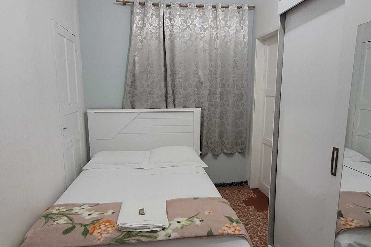 Un dormitorio con cama, armario y ventana con cortinas.
