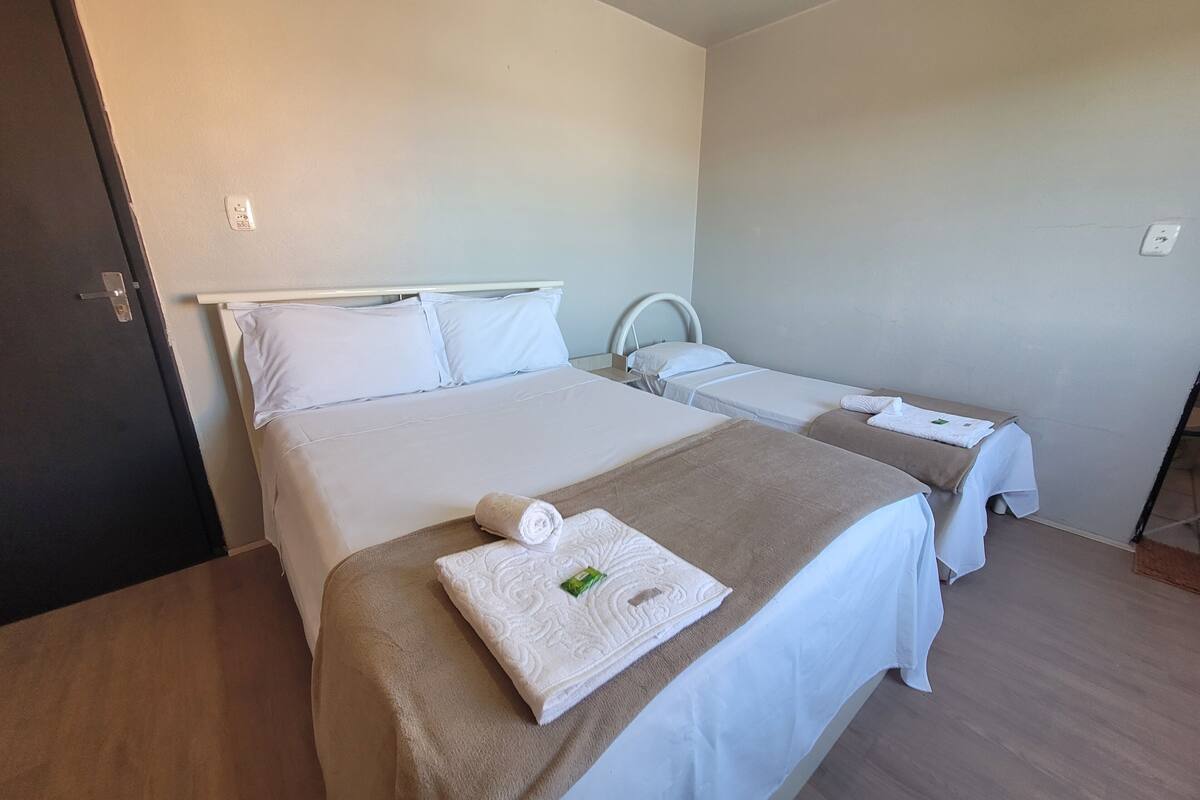 Habitación de hotel con dos camas, cada una con ropa blanca y una manta marrón. Hay una toalla sobre la cama en primer plano.