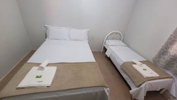 Quarto pequeno e limpo com duas camas, cada uma com colchão e almofadas brancas e um cobertor marrom. Há toalhas sobre as camas.