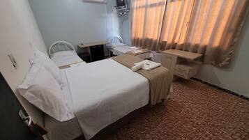 Quarto de hotel com duas camas, uma escrivaninha, uma cadeira, uma televisão e uma janela com cortinas.