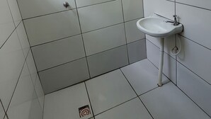 Baño con azulejos blancos, ducha, lavamanos y espejo.