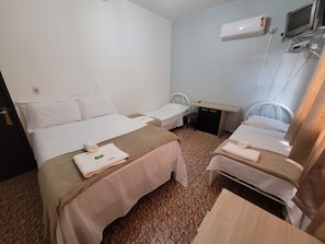 Une chambre d’hôtel avec deux lits, un bureau, une chaise, un appareil de climatisation et un téléviseur.