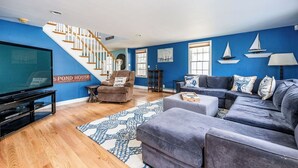 A living room with a blue wall, a staircase, a large TV, a sofa, and a chair. - Beautiful waterfront home- mins to beach, fishing /kayak right from the backyard (Yarmouth)