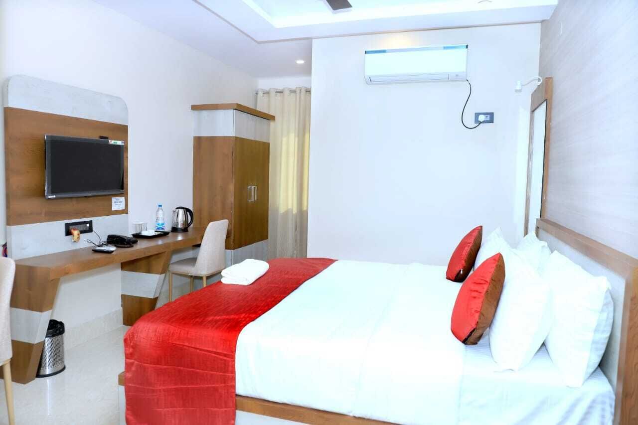 A hotel room with a bed, a desk with a computer, a chair, a TV, and a window.