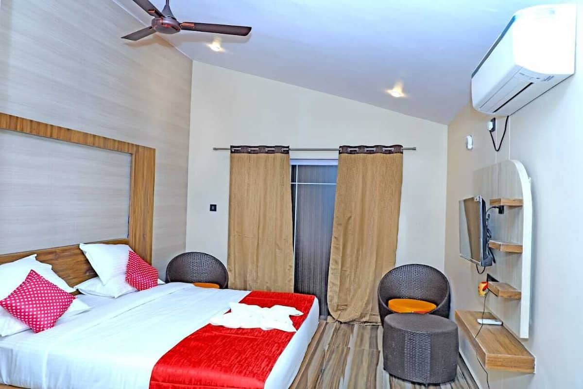 A hotel room with a bed, two chairs, a TV, and an air conditioning unit.