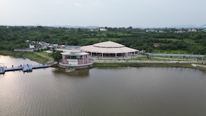 A riverside building with a circular central structure, connected by a bridge to a dock with boats.