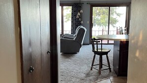 Un couloir mène à une salle à manger avec vue sur l’extérieur, où se trouvent une chaise et une table.