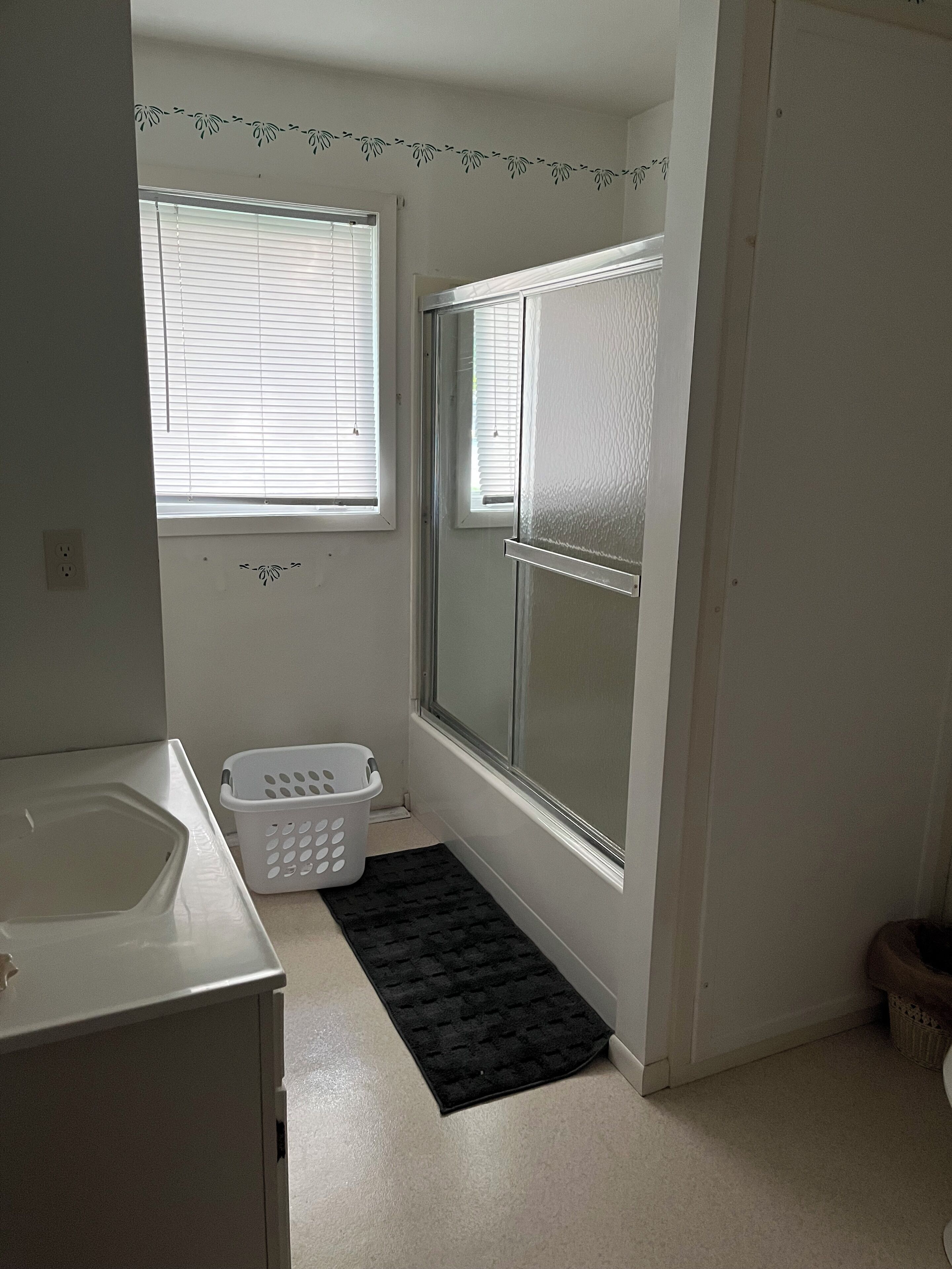 Een badkamer met een douche, toilet, wastafel en een raam met jaloezieën.