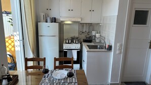 A compact kitchen with a refrigerator, stove, and sink. There is a dining table with chairs and a glass of red wine. - Zen Studio 2 min from the beach with a spacious veranda, free WiFi, and A/C. (Rethymno)
