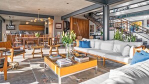 A spacious living area with a modern sofa, wooden chairs, a coffee table, and a staircase leading to an upper level.