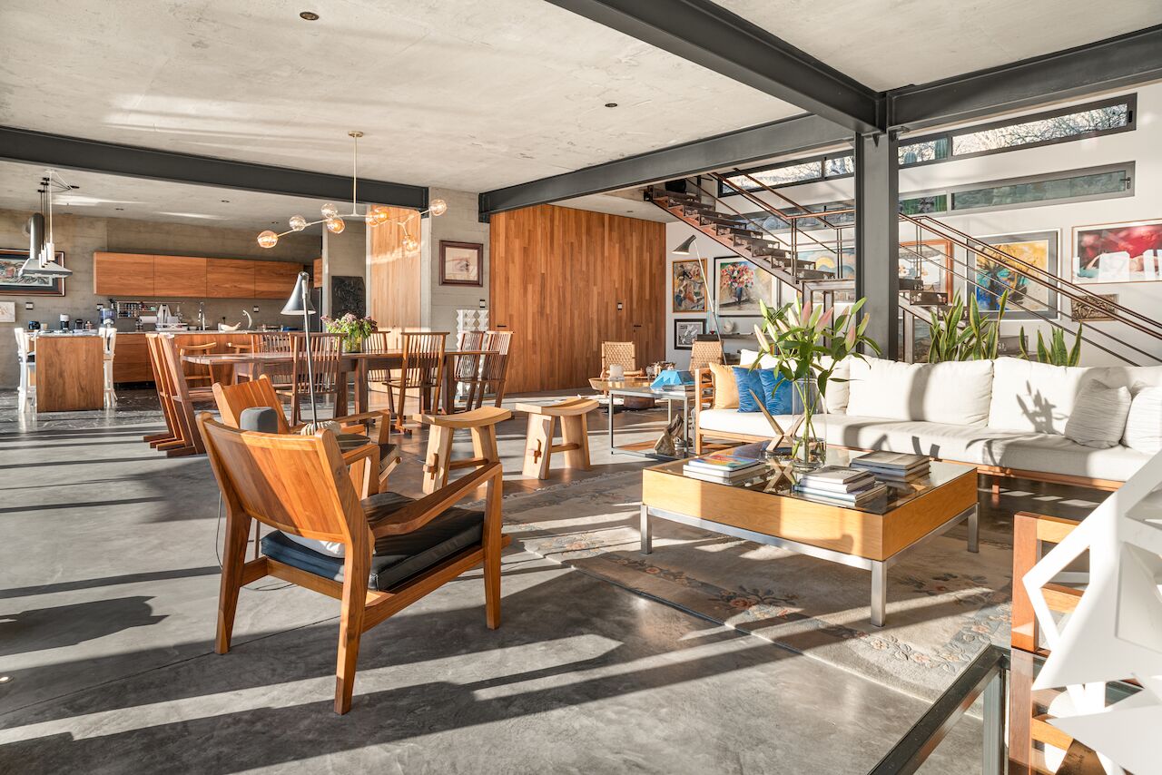 A spacious living area with a dining set, a sofa, and a coffee table. There is a staircase leading to an upper level.