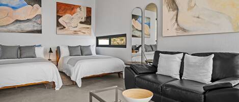 A modern bedroom with two beds, a black leather sofa, and abstract paintings on the walls.