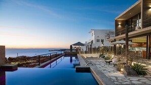 A modern hotel with a pool overlooking the sea, stone pathways, and outdoor seating.