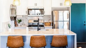 Une cuisine moderne avec des meubles blancs, un réfrigérateur en acier inoxydable et un îlot central doté de tabourets de bar.