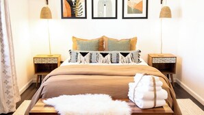 Une chambre bien rangée, avec un lit, deux tables de chevet et trois œuvres d’art encadrées accrochées au mur.