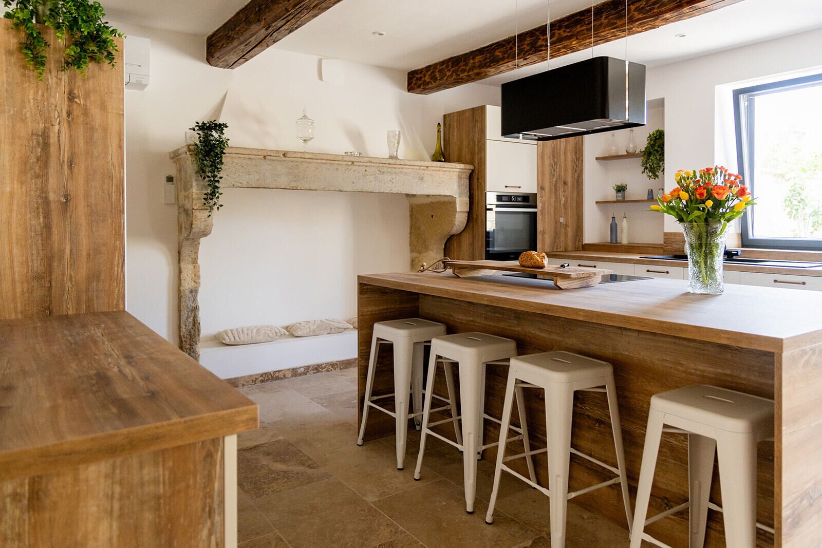 Une cuisine avec un îlot central en bois, des tabourets de bar, un four encastré et une grande fenêtre.