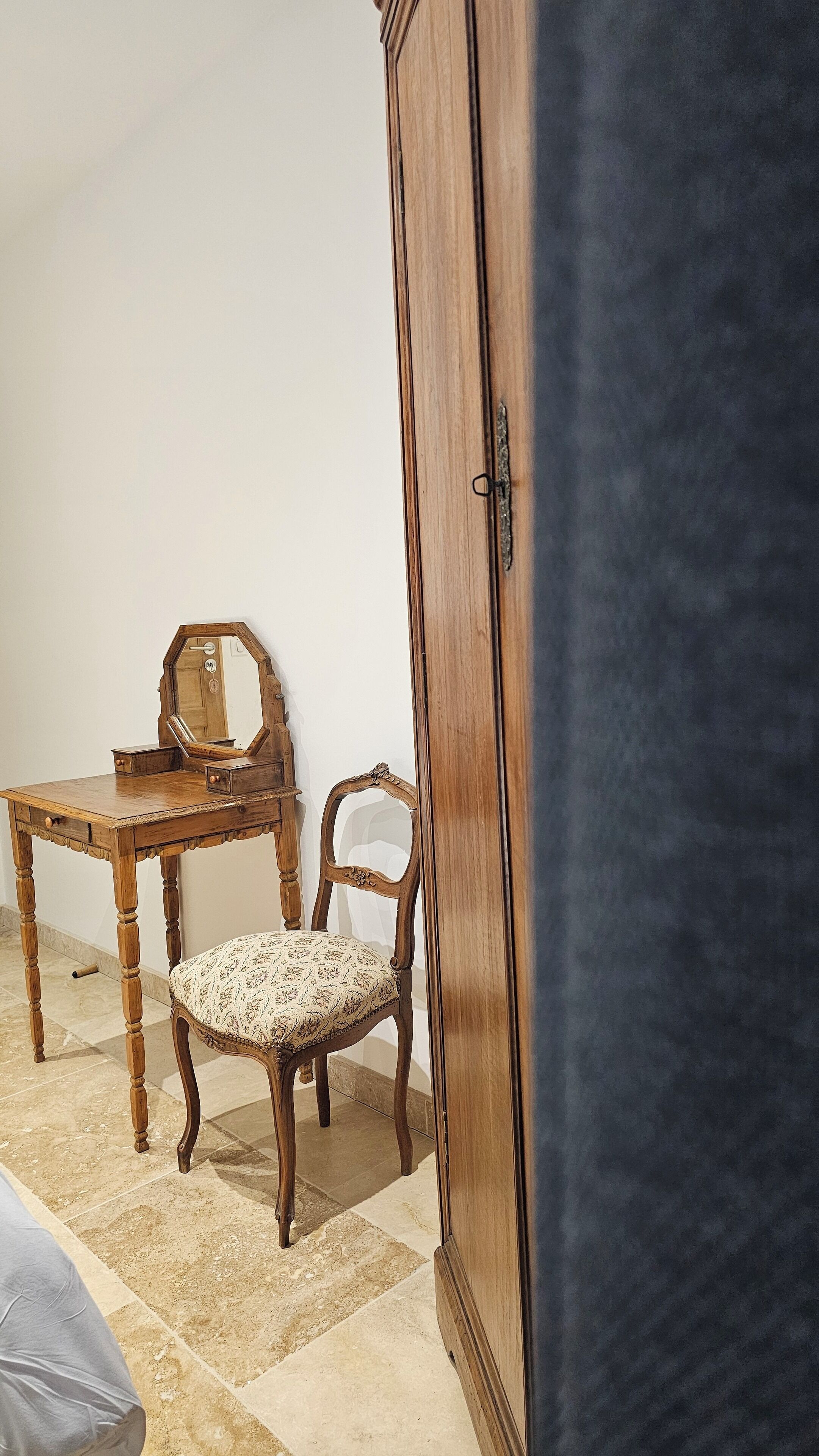 A room with a wooden cabinet, a small table with a mirror, a chair, and a bed.