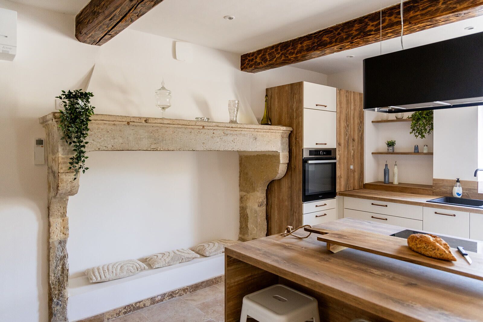 A kitchen with a stone fireplace, wooden beams, a countertop, and a sink.