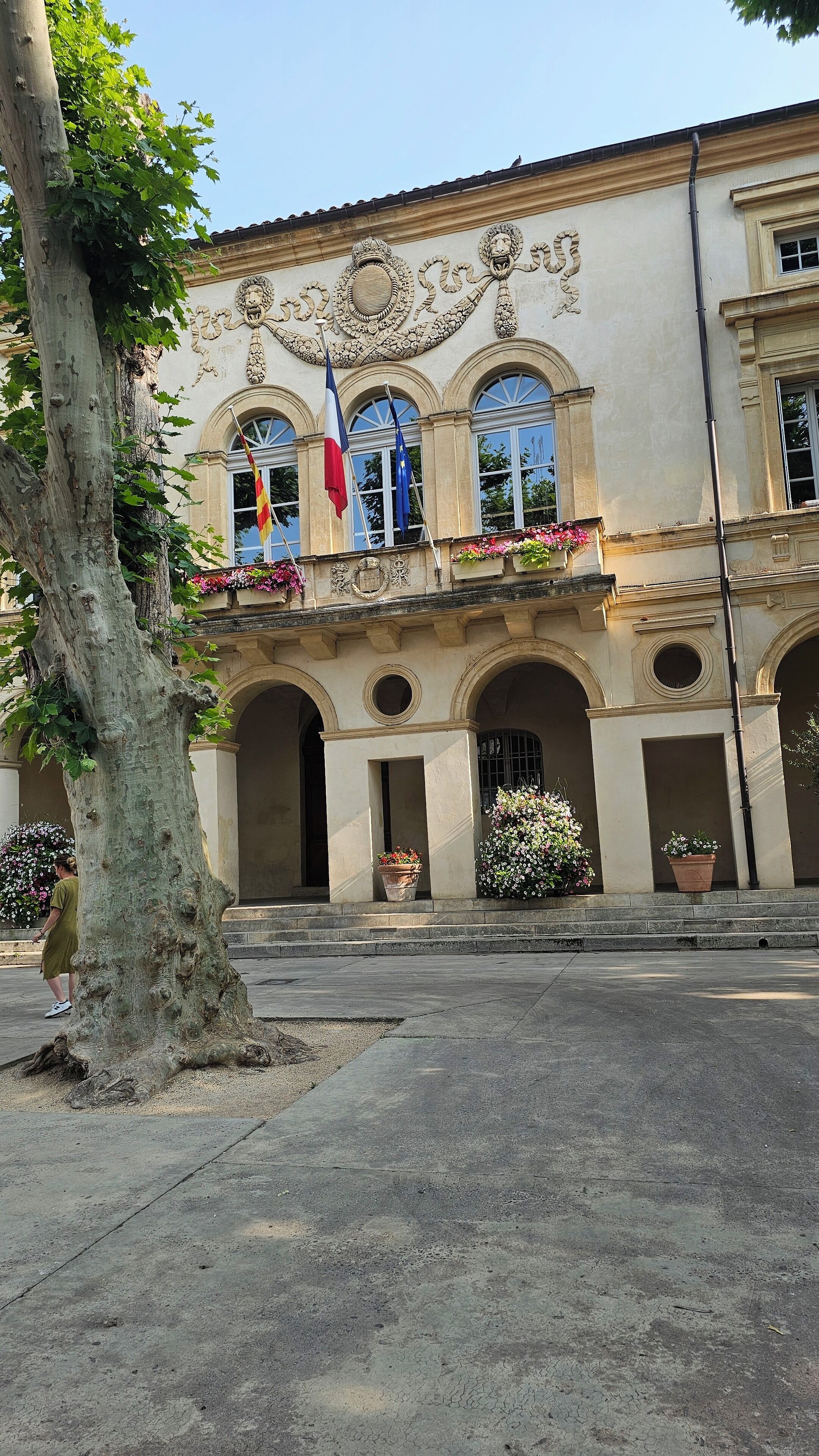 Un bâtiment à la façade classique, doté de fenêtres en arc de cercle et d’un balcon orné de jardinières.