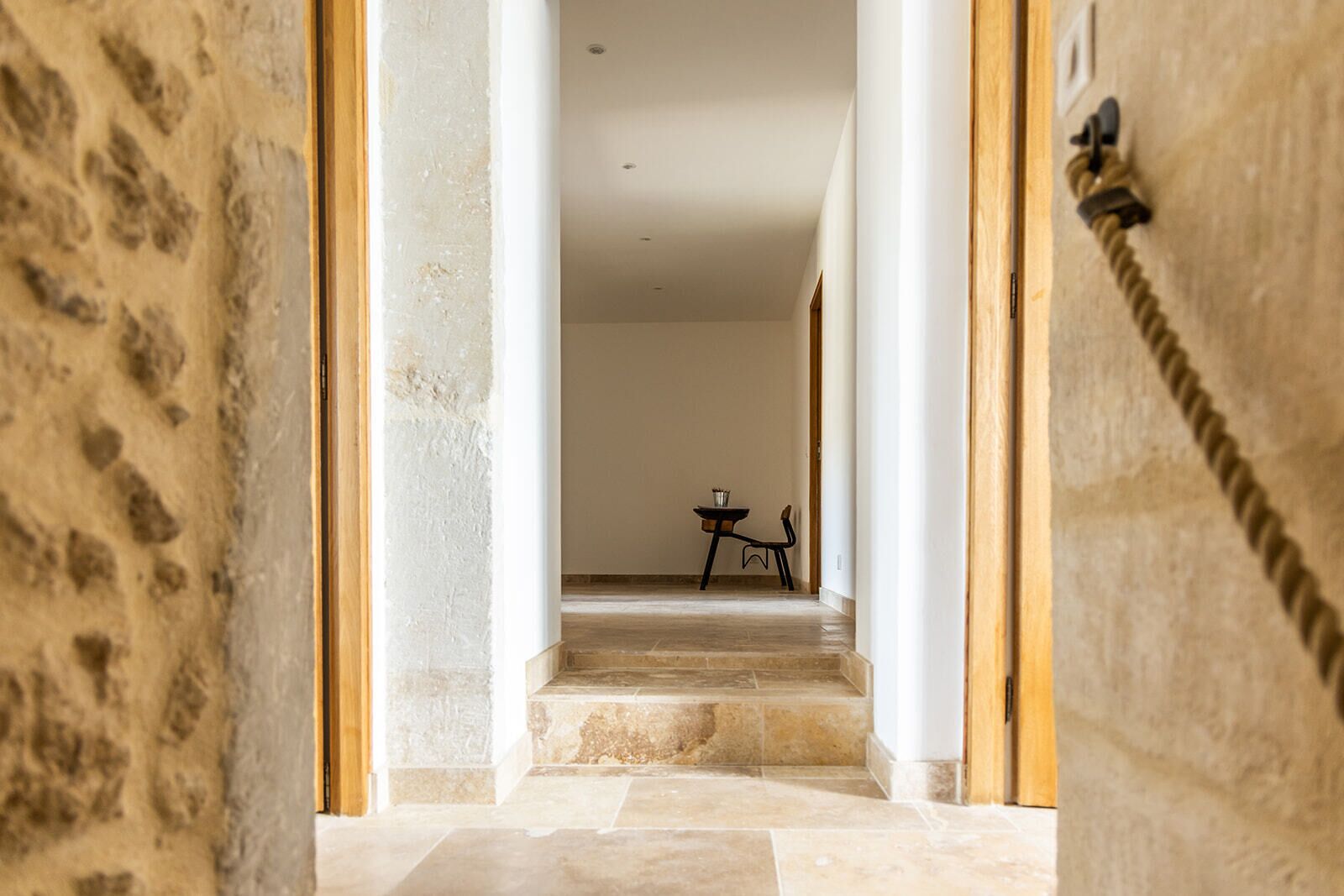 Un couloir aux murs de pierre, une porte en bois et une petite table avec une chaise.
