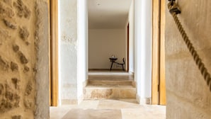 Un couloir aux murs de pierre, une porte en bois et une petite table avec une chaise.