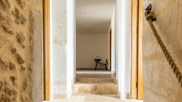 Un couloir aux murs de pierre, une porte en bois et une petite table avec une chaise.