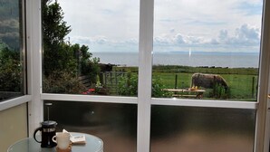 Ein Zimmer mit Glastür, die auf einen Balkon führt, einem kleinen Tisch mit Kaffeekanne und Tasse sowie einem Stuhl.