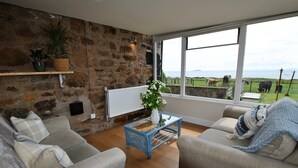 Ein Wohnzimmer mit Steinwand, Blick auf einen Bauernhof und einer Couch mit Strickdecke.