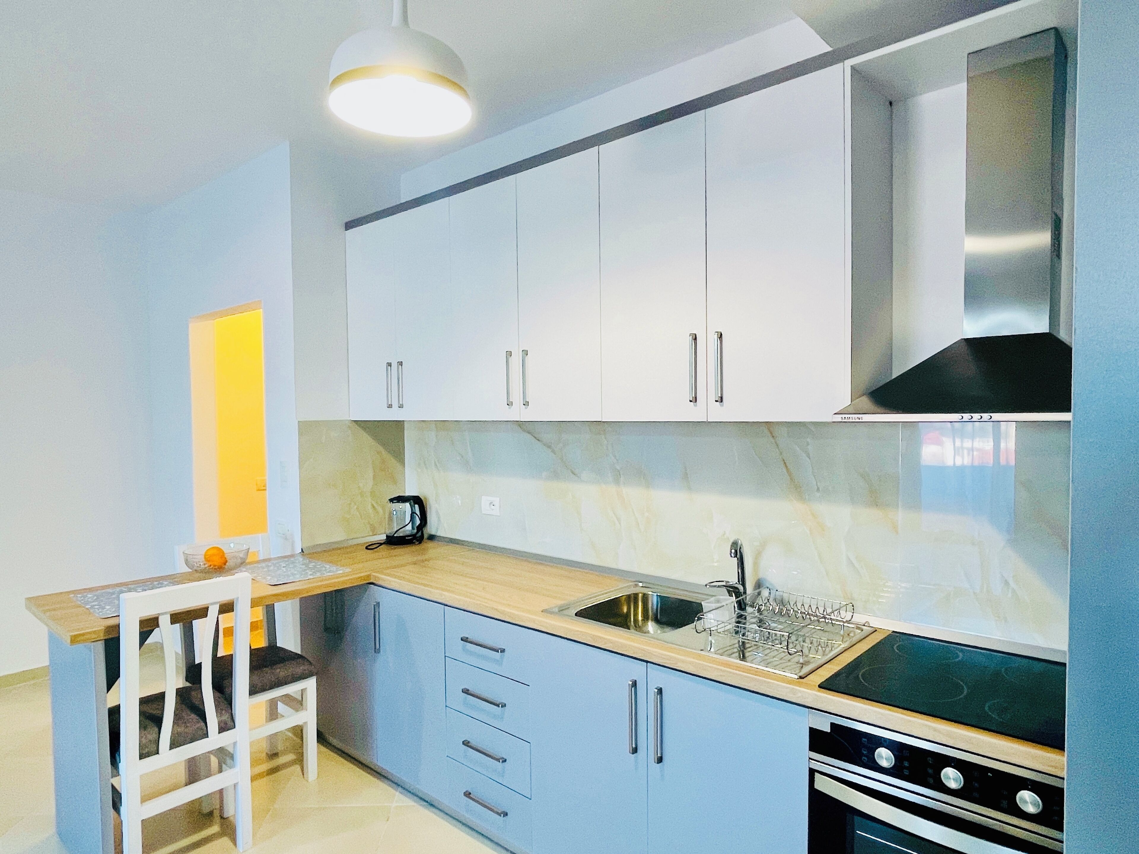 Une cuisine moderne avec des meubles blancs, un plan de travail en bois, une cuisinière encastrée et un évier.