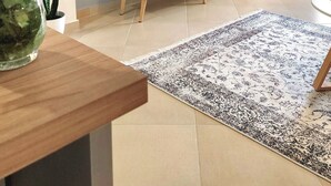Ein modernes Wohnzimmer mit einem Flachbildfernseher auf einem Holz-TV-Möbel, einer Topfpflanze und einem dekorativen Teppich.
