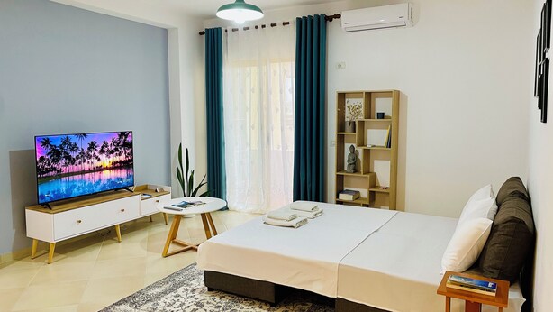 Ein Hotelzimmer mit Bett, Fernseher, kleinem Tisch, Bücherregal und einem Fenster mit Vorhängen.