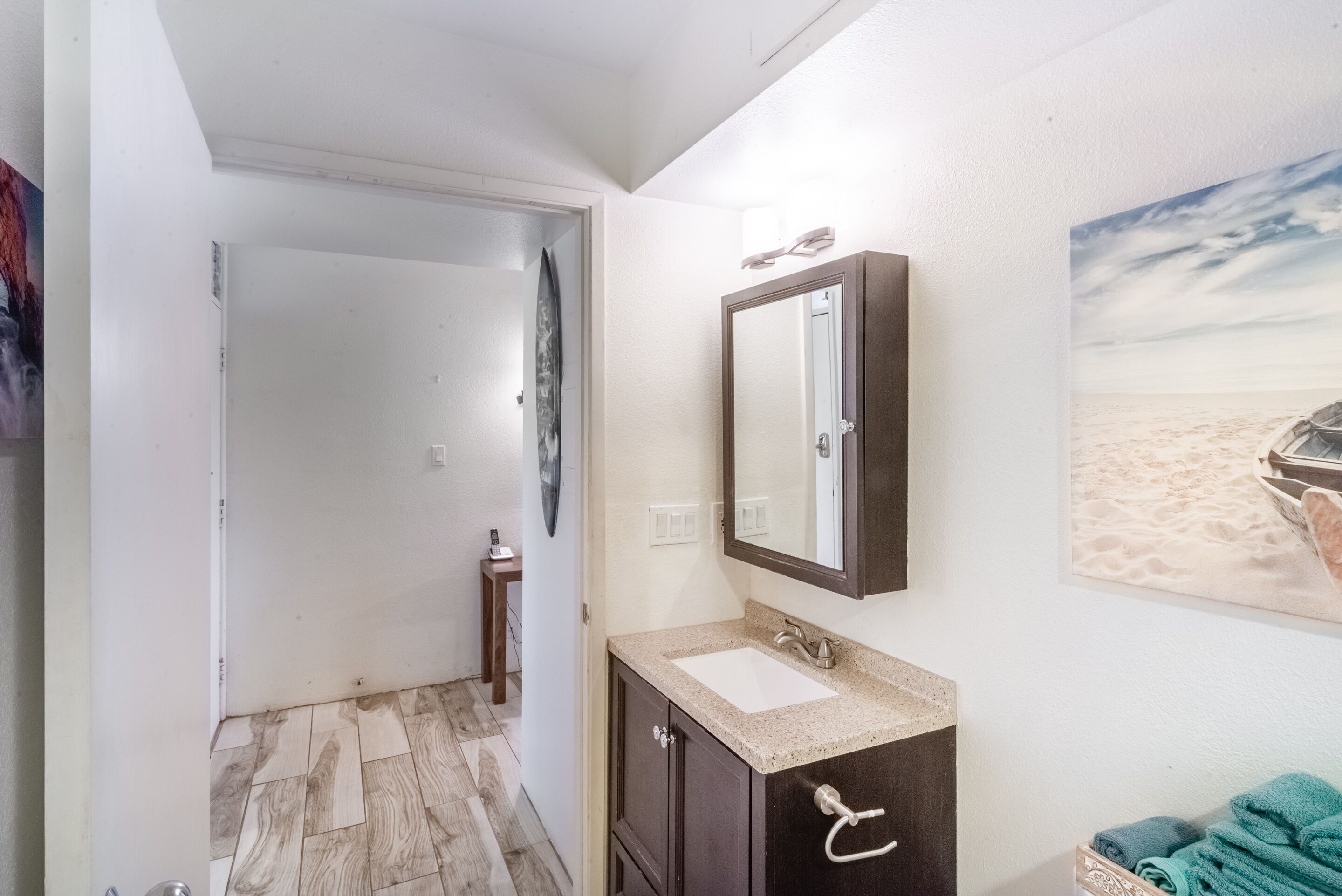 Un baño con suelo de madera, un lavabo con espejo y un perchero para toallas.