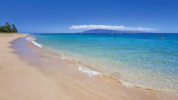 A beach with clear turquoise water, a sandy shore, and a distant mountain. - Wonderful South Maui Beach Condos  (Kihei)