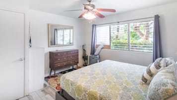 A bedroom with a bed, a ceiling fan, a window with curtains, a dresser, and a mirror.
