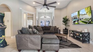 A living room with a sectional sofa, a coffee table, a TV, and a ceiling fan. - Delray Castle-Minutes to the beach and Atlantic Ave (Delray Beach)