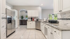 A modern kitchen with white cabinetry, a stainless steel refrigerator, a built-in dishwasher, and a marble backsplash. - Delray Castle-Minutes to the beach and Atlantic Ave (Delray Beach)