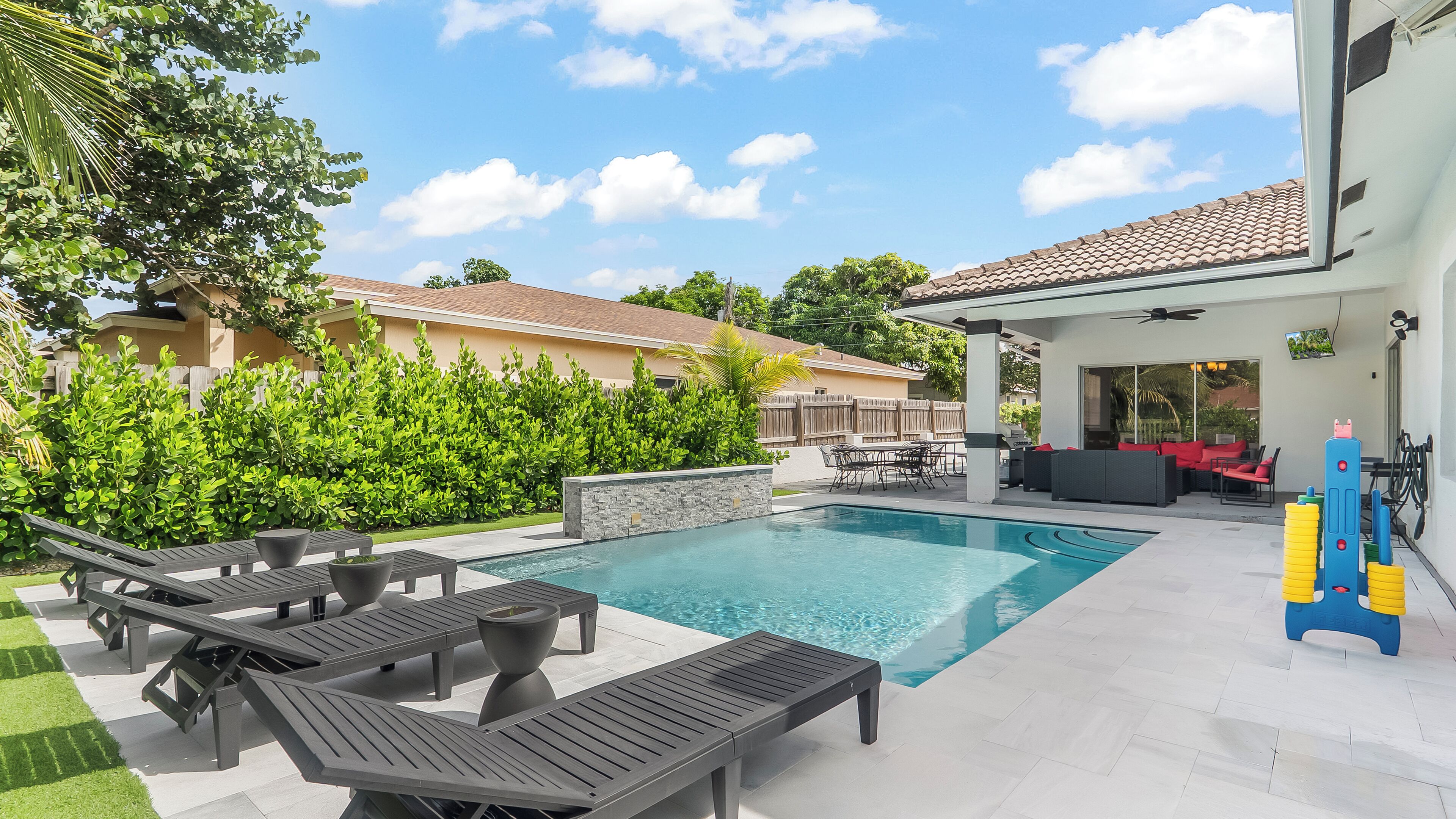 A backyard with a swimming pool, lounge chairs, and a covered patio area.